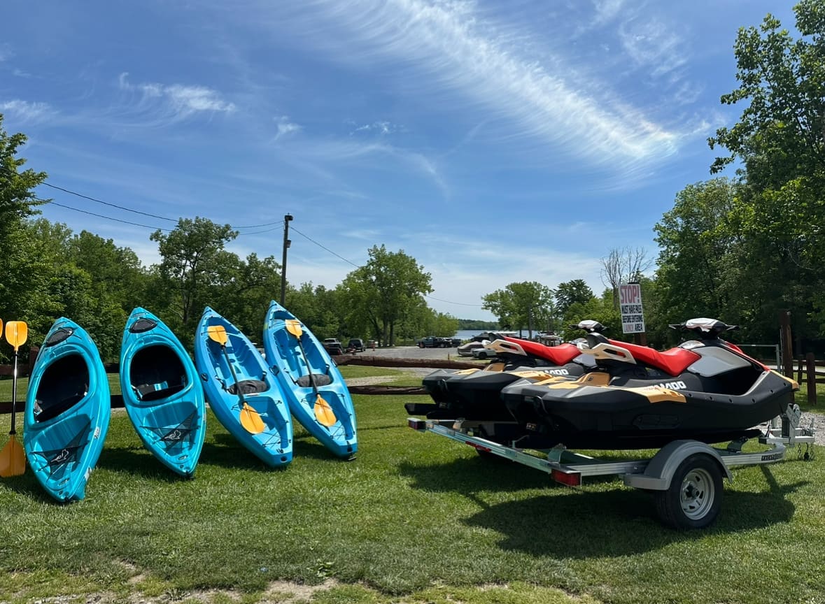 Kayaks Four blue kayaks lined up along a stand. Nearby, two black and red sea doo jet skis are on the right.